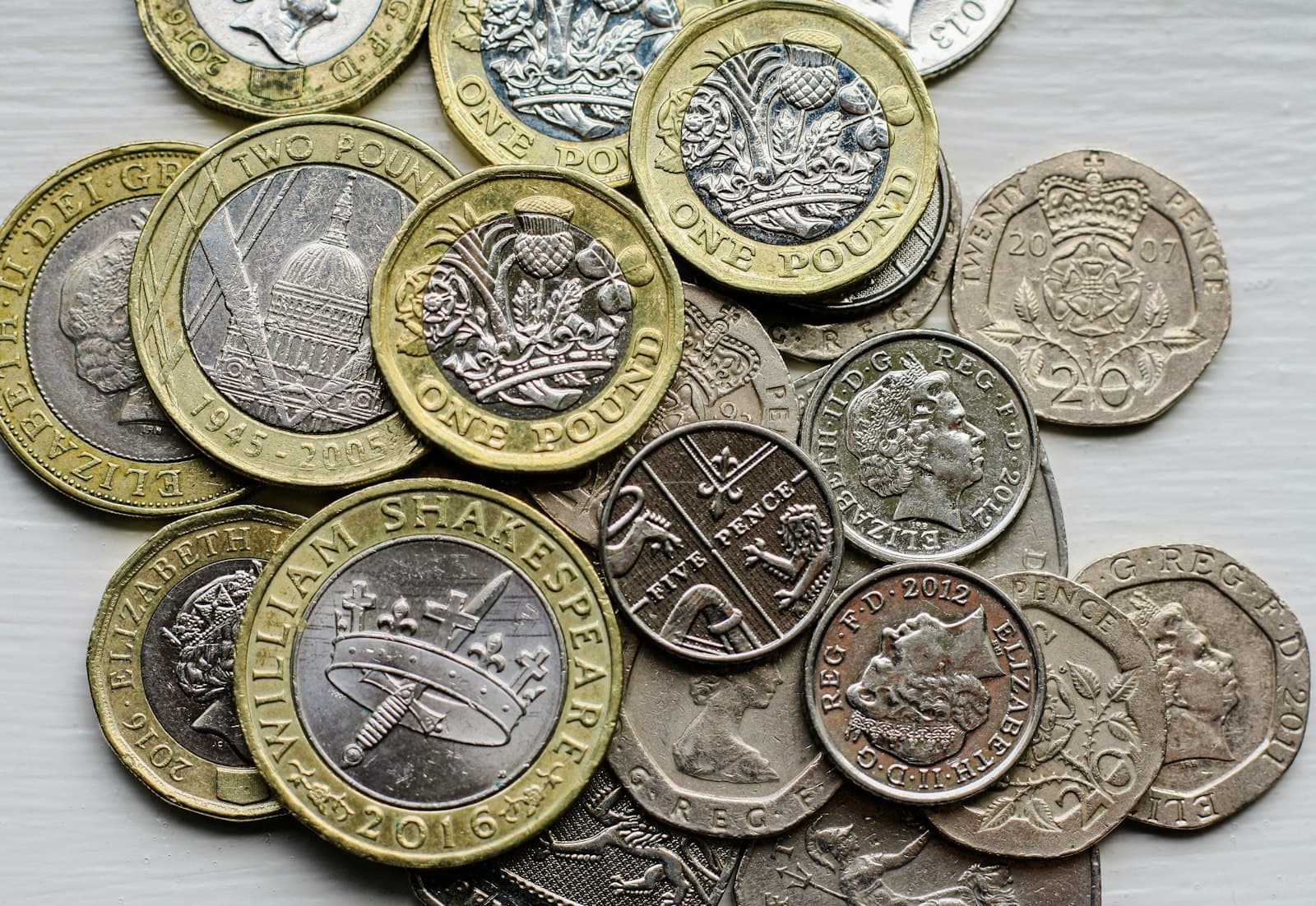 A small pile of British pound and pence coins spread out on a pale wooden surface