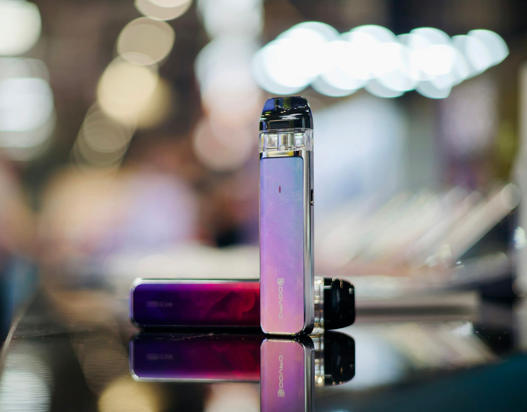Two compact rechargeable pod vape kits standing on a reflective surface, one showing its USB-C charging port
